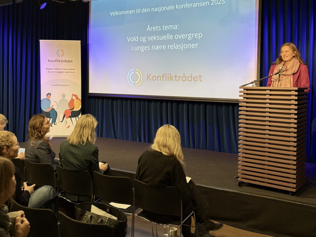Direktøren for Konfliktrådet på scene ved et podie med mennesker som ser på.